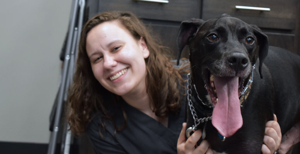 Smiling Caris College Vet Assistant student hugging black dog