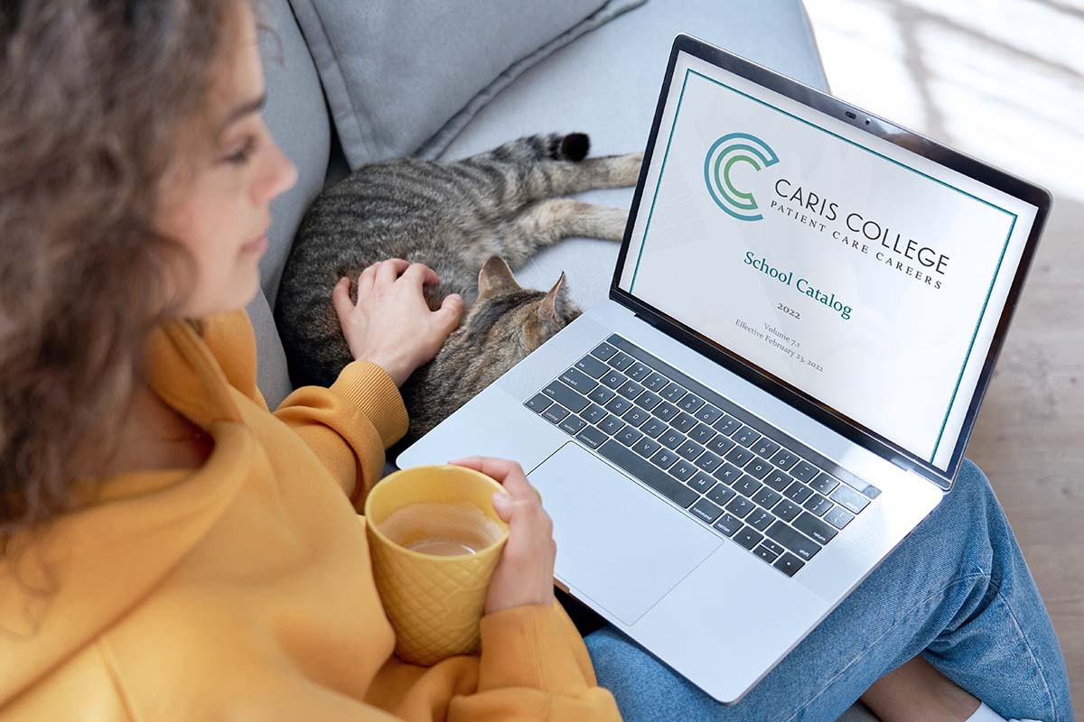 Young woman sitting on couch with cat looking at Caris College online catalog
