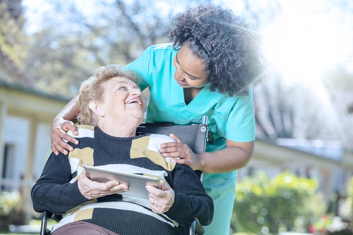 Practical nurse leaning over the shoulder of patient in wheelchair outdoors
